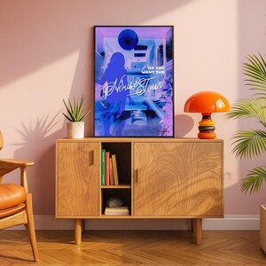 K&ouml;nnte beinhalten: Ein gerahmtes Poster mit blauem und lila Design, mit dem Text "Do You Want The House Tour". Das Poster wird auf einem Holzschrank ausgestellt, zusammen mit einer orangefarbenen Lampe und einer Topfpflanze. Der Raum hat eine moderne &Auml;sthetik aus der Mitte des Jahrhunderts.