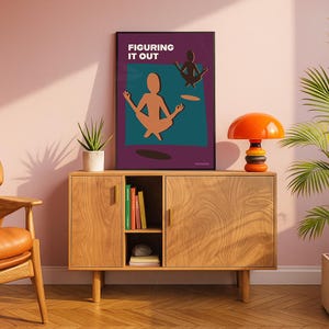 May include: A framed art print with the text "FIGURING IT OUT" features a meditating figure in a yoga pose. The artwork is displayed on a wooden cabinet with an orange lamp and a potted plant. The cabinet has two doors and a shelf with books.
