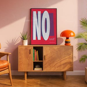 May include: A framed art print with the word "NO" in large white letters on a red background. The text "is a full sentence" is below the word "NO". The print is displayed above a wooden cabinet with an orange lamp and a potted plant.