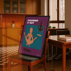 May include: A framed poster with the text "FIGURING IT OUT" in white capital letters. The poster features two stylized figures in yoga poses, one in peach and the other in dark brown, set against a teal and purple background. The poster is propped on a wooden chair.