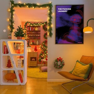 Op de afbeelding: Een gezellige interieursc&egrave;ne met kerstversiering. Een witte geometrische plank toont boeken en ornamenten. Een ingelijste poster leest "THE FUCKING LAUNDRY". Een versierde kerstboom en een krans dragen bij aan de feestelijke sfeer. Een stoel met een geel kussen staat vooraan.