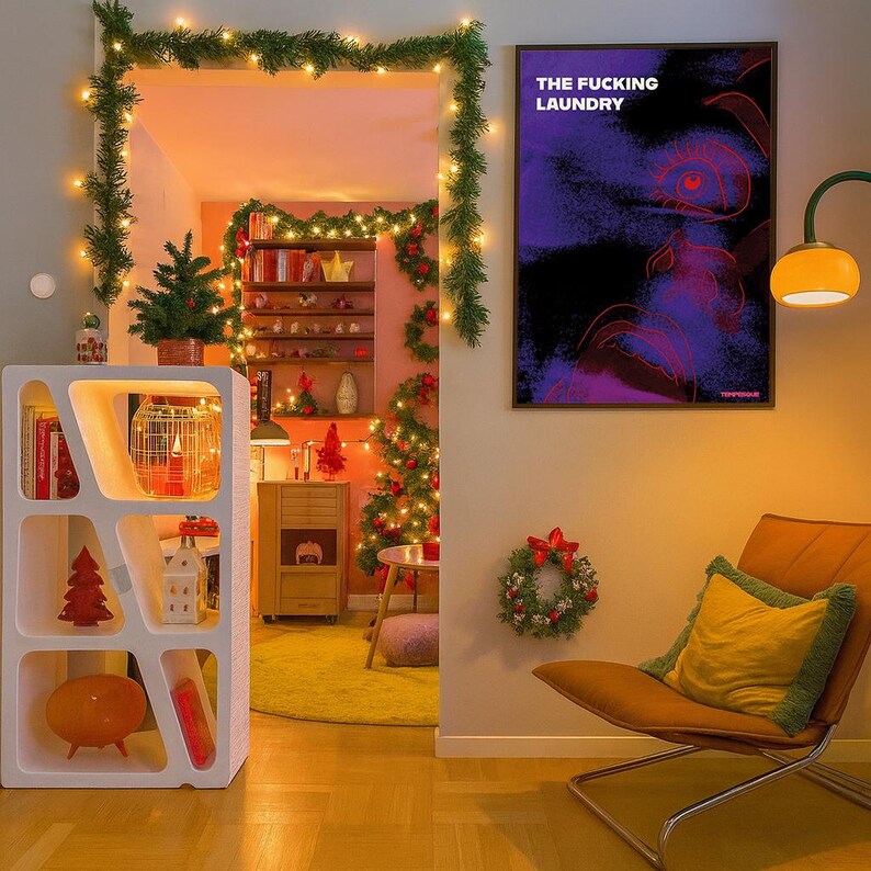 Op de afbeelding: Een gezellige interieursc&egrave;ne met kerstversiering. Een witte geometrische plank toont boeken en ornamenten. Een ingelijste poster leest "THE FUCKING LAUNDRY". Een versierde kerstboom en een krans dragen bij aan de feestelijke sfeer. Een stoel met een geel kussen staat vooraan.