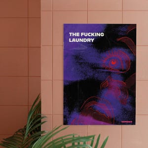 Può includere: Un poster con la scritta "THE FUCKING LAUNDRY" in bianco, su un design astratto viola e nero. L'opera presenta un disegno a linee rosse di un volto ed è montata su una parete piastrellata rosa.