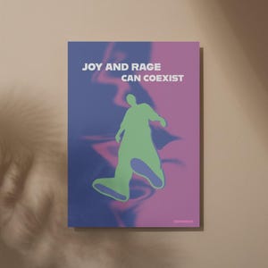 May include: A poster with the text "JOY AND RAGE CAN COEXIST" in white. The poster features a green silhouette of a person walking against a blue and pink background. The poster is rectangular and mounted on a beige wall.