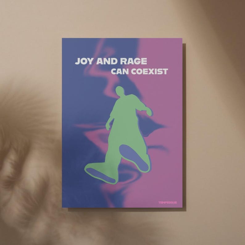 May include: A poster with the text "JOY AND RAGE CAN COEXIST" in white. The poster features a green silhouette of a person walking against a blue and pink background. The poster is rectangular and mounted on a beige wall.