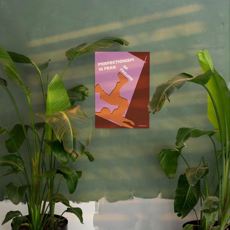 K&ouml;nnte beinhalten: Ein gerahmter Kunstdruck mit dem Text "PERFECTIONISM IS FEAR OF FAILURE" in Wei&szlig;. Das Kunstwerk zeigt eine orangefarbene Silhouette einer st&uuml;rzenden Person vor einem lila-braunen Hintergrund. Der Druck wird an einer gr&uuml;nen Wand gezeigt, umgeben von gr&uuml;nen Pflanzen.