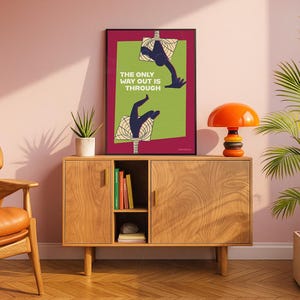 K&ouml;nnte beinhalten: Ein gerahmter Kunstdruck mit dem Text "THE ONLY WAY OUT IS THROUGH" weist ein gr&uuml;nes und bordeauxfarbenes Farbschema auf. Das Kunstwerk zeigt stilisierte H&auml;nde, die durch geometrische Formen greifen. Der Druck wird auf einem Holzschrank mit einer Retro-Orangenlampe ausgestellt.