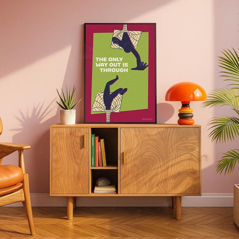 K&ouml;nnte beinhalten: Ein gerahmter Kunstdruck mit dem Text "THE ONLY WAY OUT IS THROUGH" weist ein gr&uuml;nes und bordeauxfarbenes Farbschema auf. Das Kunstwerk zeigt stilisierte H&auml;nde, die durch geometrische Formen greifen. Der Druck wird auf einem Holzschrank mit einer Retro-Orangenlampe ausgestellt.