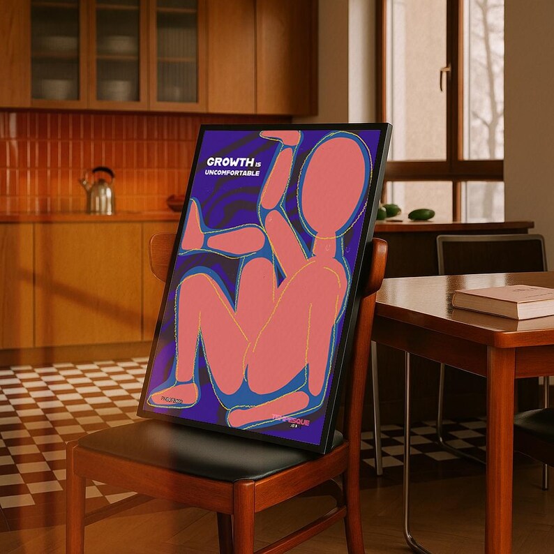 May include: A framed art print featuring a stylized human figure in shades of pink and blue against a dark purple background. The text "GROWTH is UNCOMFORTABLE" is displayed at the top. The artwork is propped on a wooden chair.