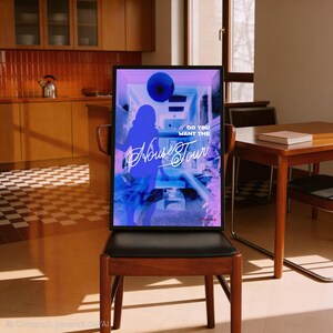 K&ouml;nnte beinhalten: Ein gerahmtes Poster mit schwarzem Rand, das ein blaues und violettes Design mit dem Text "Do You Want The House Tour" zeigt. Das Poster steht auf einem Holzstuhl mit schwarzem Sitz in einem Raum mit K&uuml;che und Esstisch.