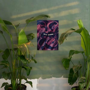 May include: A framed art print with a swirling abstract design in shades of pink and navy blue. The text "DO IT SCARED" is centered on the print. The artwork is displayed on a green wall, surrounded by lush green plants.