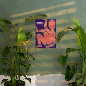 May include: A poster with a purple background features an abstract orange figure with blue outlines. The text "GROWTH. UNCOMFORTABLE" is printed in white. The poster is displayed on a green wall, surrounded by lush green plants.