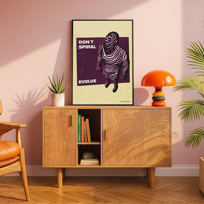 May include: A framed art print with the words "DON'T SPIRAL EVOLVE" and a graphic of a figure with zebra-like stripes. The print is displayed on a wooden cabinet with an orange mushroom lamp and a potted plant.