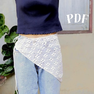 May include: A white, open-weave crochet wrap skirt with a triangular shape, tied at the waist. The skirt is worn over blue jeans and paired with a navy blue top. The word "PDF" is visible in the upper right corner.