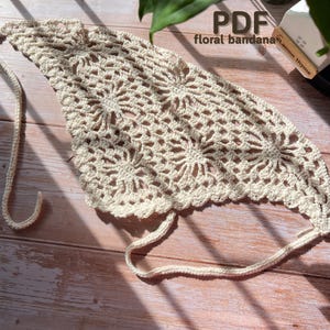 May include: Cream-colored, crocheted bandana with a floral pattern. The bandana has a triangular shape with a scalloped edge and ties. The text "PDF floral bandana" is visible in the upper right corner.