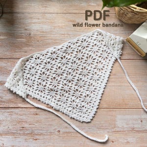Puede incluir: Un pañuelo blanco tejido a ganchillo con un patrón floral y cierre de cordón. El texto "PDF wild flower bandana" es visible en la imagen. El pañuelo está hecho de un material suave y de tejido abierto.