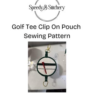 May include: A golf tee clip-on pouch sewing pattern. The pouch is white with a green border and a red golf tee inside. The pouch has a gold-colored clasp and a key ring. The text "Speedy B Stitchery" is at the top.