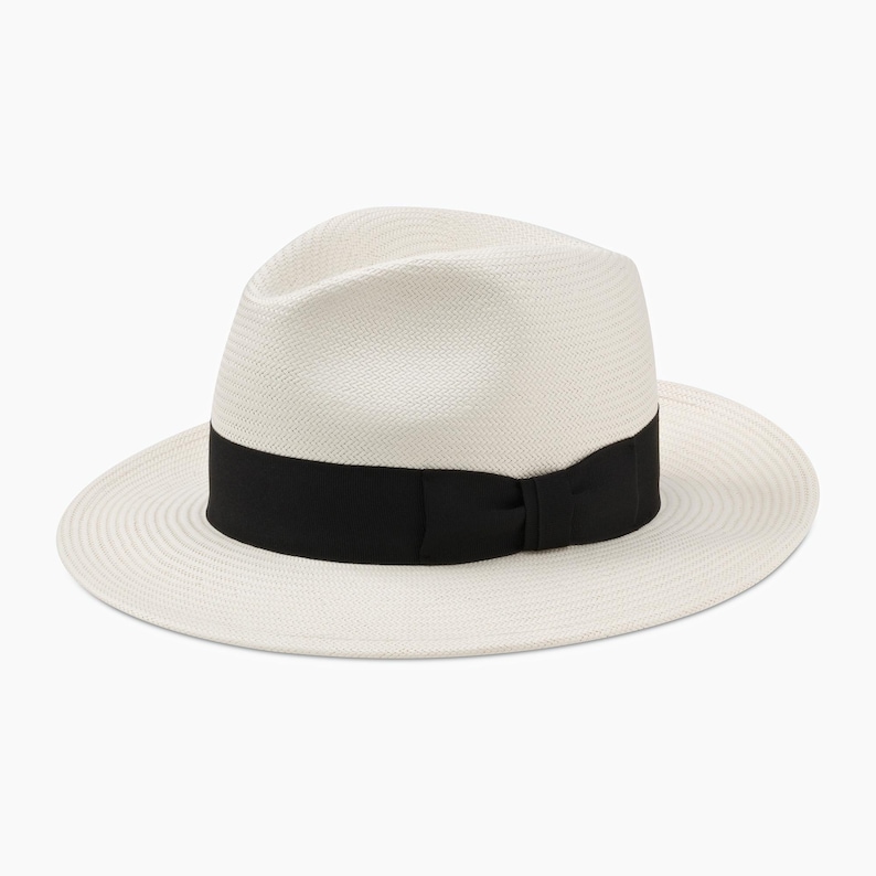 K&ouml;nnte beinhalten: Ein wei&szlig;er Strohhut im Fedora-Stil mit einem schwarzen Band um die Krone.