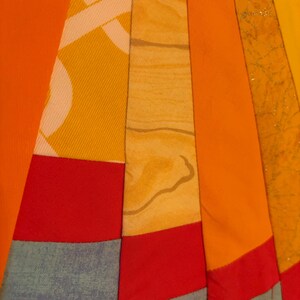 May include: A quilt featuring a radial pattern of fabric strips in shades of orange, yellow, and red, interspersed with light blue sections. The fabric textures include solid colors, a white geometric print, a wood grain pattern, and gold glitter.