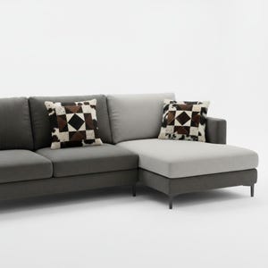May include: A grey sectional sofa with two patterned cushions. The cushions have a geometric design with brown, black, and white cowhide patches. The sofa features a chaise lounge and is in shades of grey.