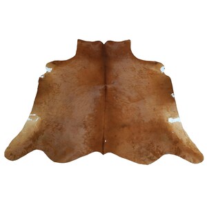 May include: A brown cowhide rug with a natural pattern and white markings. The rug has a soft texture and a unique shape, suitable for adding warmth and style to any room. The hide is a rich, earthy brown color.