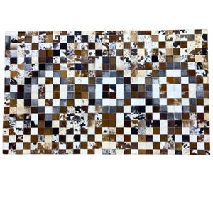 K&ouml;nnte beinhalten: Ein rechteckiger Kuhfellteppich mit Patchwork-Design. Der Teppich hat ein Schachbrettmuster aus verschiedenen Braunt&ouml;nen, Wei&szlig; und schwarzen Quadraten. Die Quadrate bestehen aus echtem Kuhfell und erzeugen ein einzigartiges und strukturiertes Aussehen.
