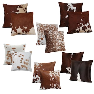 May include: A collection of square throw pillows featuring various cowhide patterns in shades of brown, white, and tan. Each pillow displays a unique animal print design with irregular spots and patches, showcasing a range of color distributions.