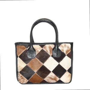 Könnte beinhalten: Eine rechteckige Tragetasche mit Patchwork-Design. Die Tasche hat einen schwarzen Lederbesatz und -griffe. Der Patchwork besteht aus rautenförmigen Teilen in Braun-, Beige- und Weißtönen. Die Tasche hat eine strukturierte Form und ein klassisches Design.