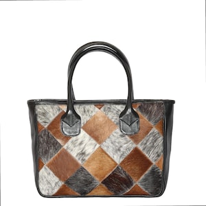 Puede incluir: Un bolso tote rectangular con un diseño de patchwork. El bolso presenta un patrón de parches en forma de diamante en tonos marrones, grises y blancos. El bolso tiene asas y ribetes de cuero negro.