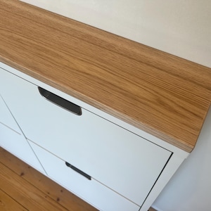 Könnte beinhalten: Ein weißer Schuhschrank mit einer Holzplatte und zwei Schubladen. Die Schubladen haben schwarze Metallgriffe.