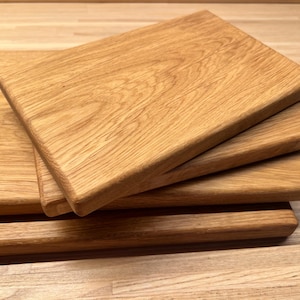 Könnte beinhalten: Ein Stapel aus vier rechteckigen Holzschneidebrettern mit abgerundeten Kanten. Jedes Brett weist eine natürliche hellbraune Holzmaserung mit sichtbarer Textur und glatter Oberfläche auf, angeordnet in einem leicht versetzten Stapel.
