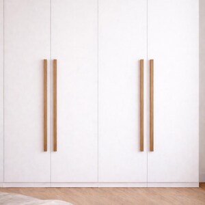 Könnte beinhalten: Ein weißer Kleiderschrank mit vier Türen und vertikalen Holzgriffen. Die Türen haben ein minimalistisches Design. Der Schrank steht vor einer hellen Wand und auf einem Holzboden.