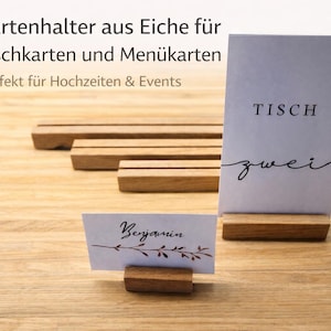 May include: Wooden table card holders with a natural finish. One holder displays a card with the word "TISCH zwei" in black script. Another displays a card with the name "Benjamin". The holders are designed for weddings and events.