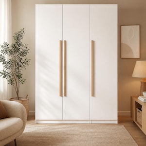 Könnte beinhalten: Ein weißer Kleiderschrank mit drei Türen und vertikalen Holzgriffen. Der Schrank steht vor einer Wand in neutralen Farbtönen. Ein Teppich und eine Topfpflanze befinden sich im Vordergrund.