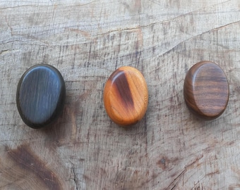 May include: Three wooden coasters in different wood grains. The coasters are round and have a smooth finish. The coasters are arranged in a row from left to right: black, brown, and orange.