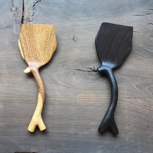 May include: Two wooden spatulas with unique branch-like handles. One spatula is light brown wood, the other is dark brown wood.