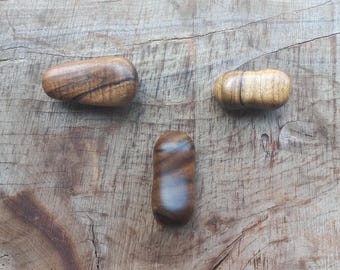 May include: Three handcrafted wooden objects with rounded shapes, each displaying unique grain patterns and varying shades of brown. The objects are arranged on a textured wooden surface, showcasing natural wood tones.