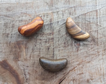 May include: Three wooden pieces in the shape of a crescent moon, with different wood grain patterns and colors. The pieces are arranged on a wooden surface.