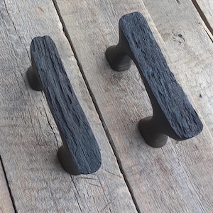 Könnte beinhalten: Zwei schwarze Holz-Schubladengriffe mit rustikalem, recyceltem Holzlook. Die Griffe haben eine einfache, rechteckige Form mit abgerundeten Kanten.