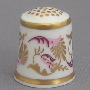 Puede incluir: Dedal de porcelana blanca con ribete dorado y diseño floral rosa y dorado.