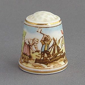 May include: A white porcelain thimble with a gold trim and a colorful scene of two people working in a field. The scene includes a tree, a fence, and a small building in the background.