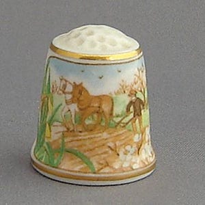 May include: A porcelain thimble with a colorful scene of a horse-drawn plow in a field. The thimble has a gold rim and a white background.