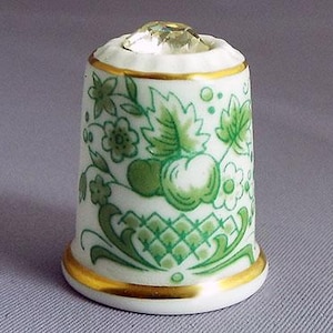 May include: A white porcelain thimble with a green floral design and a clear crystal top.