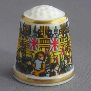 May include: A white porcelain thimble with a gold trim and a colorful image of a castle with flags and people. The thimble is a collectible item.