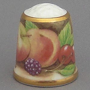 May include: A porcelain thimble with a gold trim and a colorful fruit design. The thimble features a peach, pear, cherries, and a blackberry.