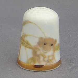 Peut inclure: Un dé à coudre en céramique blanche avec un bord doré et une image peinte d'une souris des champs brune sur une tige de blé.