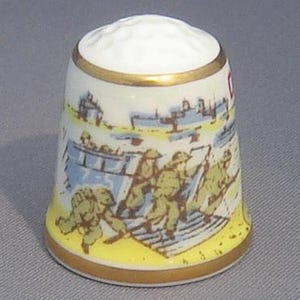 May include: A white porcelain thimble with a gold rim and a colorful illustration of soldiers landing on a beach. The thimble features the text "D-Day 1944".