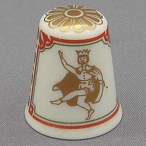 Könnte beinhalten: Eine weiße Porzellan-Fingerhut mit einem goldenen und roten Design. Der Fingerhut zeigt ein stilisiertes Bild einer Person mit einer Krone und einem Umhang, die tanzt.