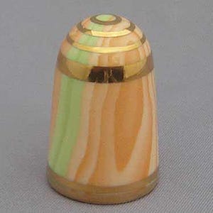 May include: A ceramic thimble with a peach and green striped pattern and gold trim. The top of the thimble has a gold and green concentric circle design.