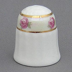 May include: White ceramic thimble with a gold trim and pink rose design.